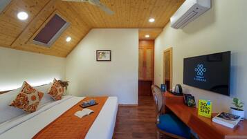 A hotel room with a wooden ceiling, a bed with a white and orange bedspread, a desk with a chair, a flat-screen TV, and a small potted plant.