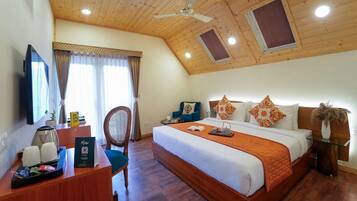 Una habitación de hotel con techo de madera, cama con ropa de cama blanca y naranja, escritorio con cafetera y televisión.