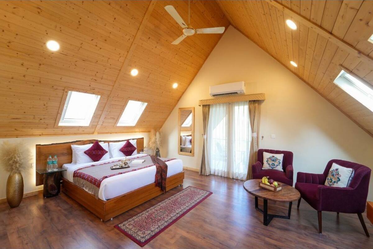 Een slaapkamer met een houten plafond, een bed, twee stoelen, een kleine tafel en een raam.