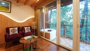 A cozy room with two plush armchairs, a small table with a book and a vase, and a large sliding glass door leading to a balcony with a hot tub. - Samsara Luxury Cottages & Spa  (Kandaghat)