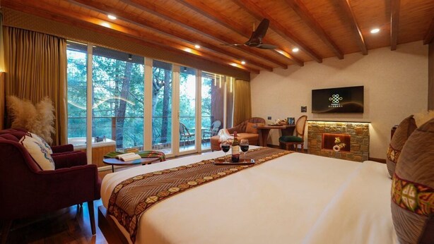 A spacious bedroom with a large bed, a fireplace, a television, and a view of the outdoors. - Samsara Luxury Cottages & Spa  (Kandaghat)