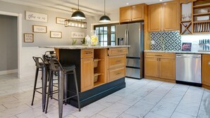 Cocina moderna con armarios de madera, electrodomésticos de acero inoxidable y una isla central con taburetes de bar.