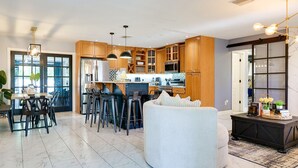 Una cocina moderna con armarios de madera, un comedor con taburetes de bar y una sala de estar con un sofá blanco grande.