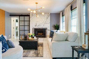 A modern living room with a fireplace, a sofa, a coffee table, and a chandelier. - Work & Unwind in North Port Fenced Yard + Cozy Lounge (North Port)