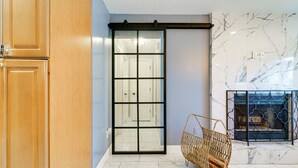 Una habitación con puerta de vidrio corredera, una silla de mimbre y chimenea con protección metálica.