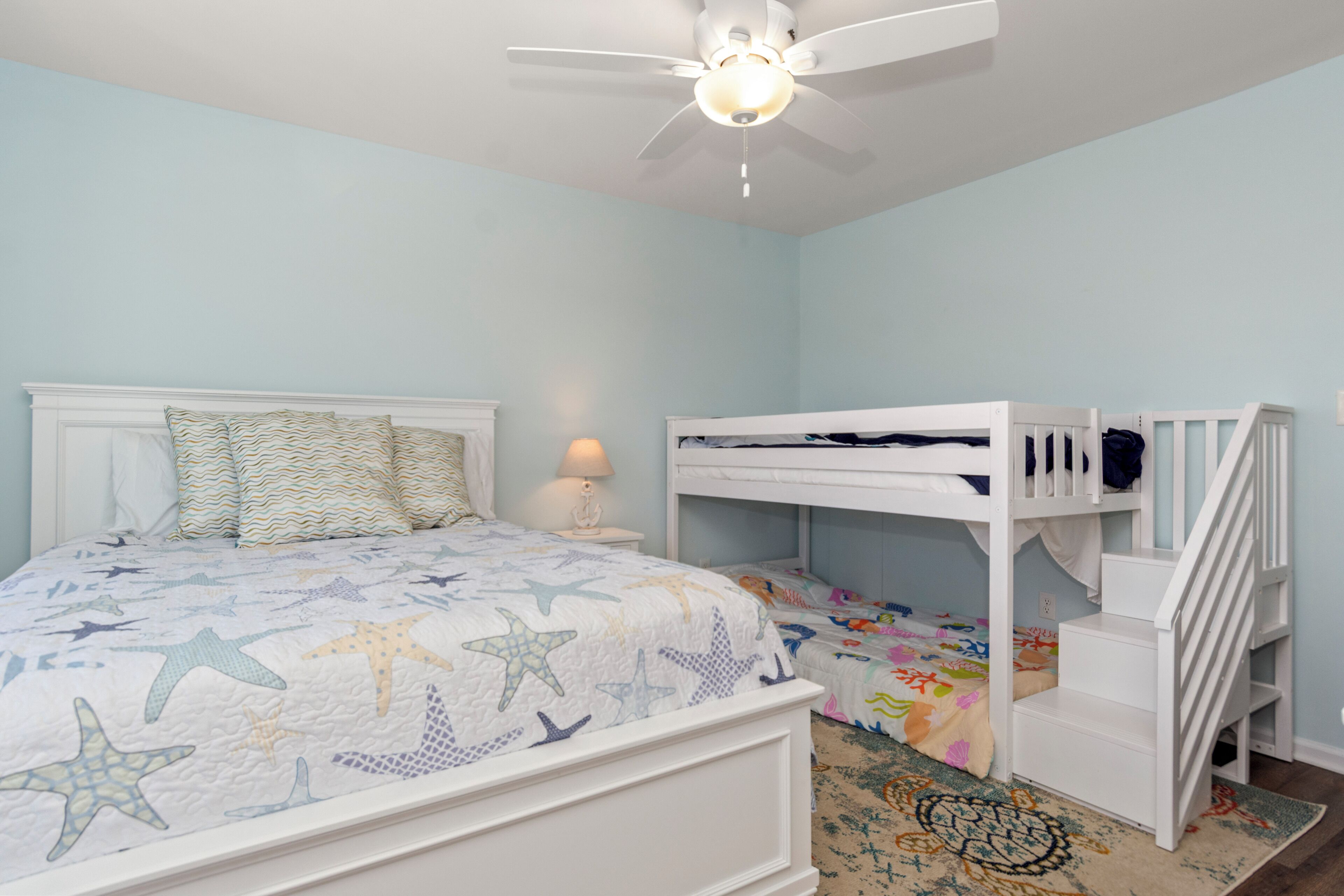 A bedroom with a bed, a bunk bed, a ceiling fan, and a nightstand with a lamp.