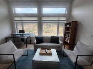 A living room with a sofa, a coffee table, a desk with a computer, and a bookshelf.
