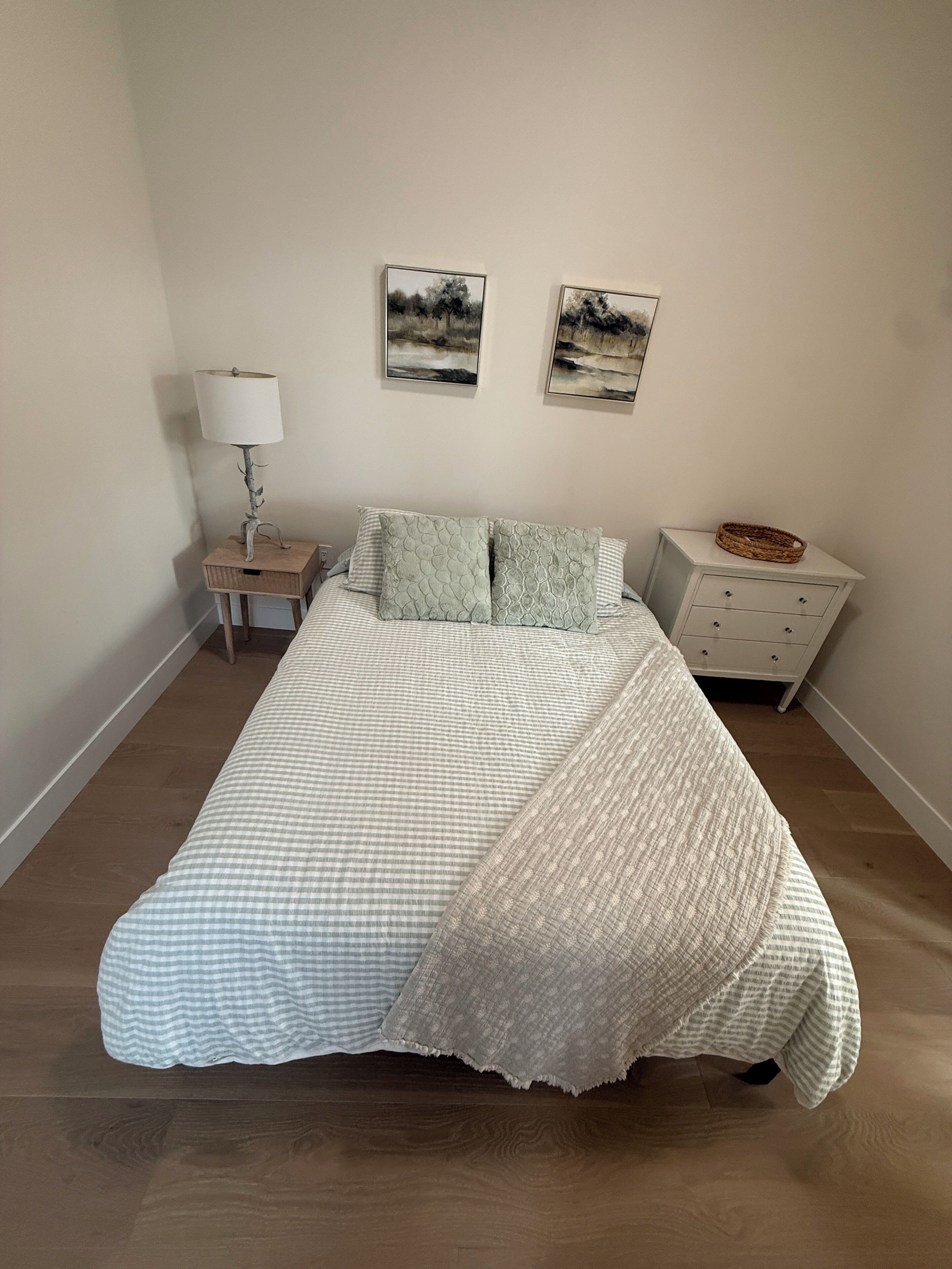 A neatly made bed with a checkered bedspread and pillows, a bedside lamp, and two framed pictures on the wall.
