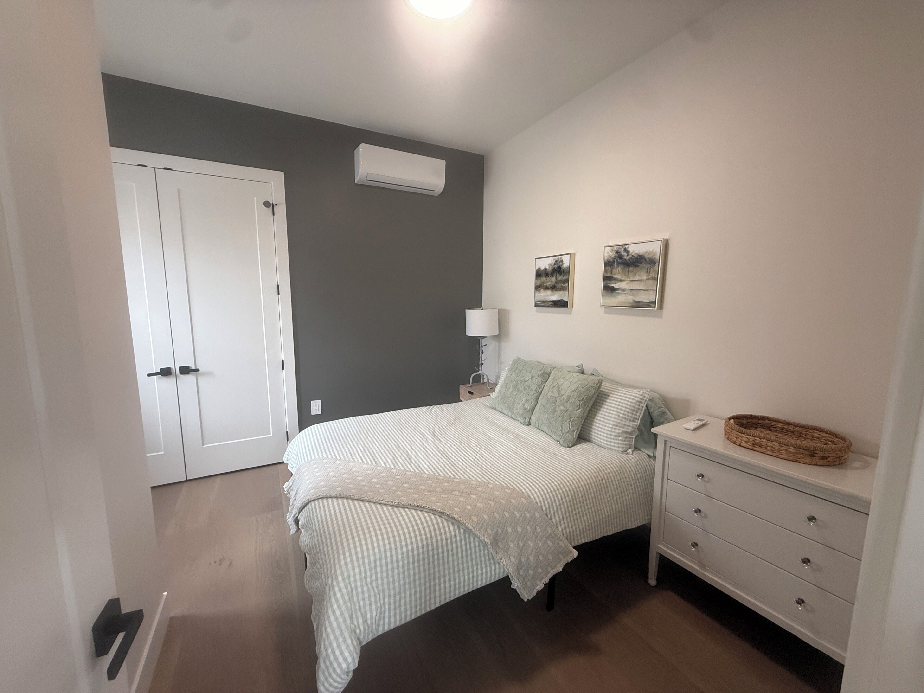 A bedroom with a bed, bedside table, lamp, and wall-mounted air conditioner.