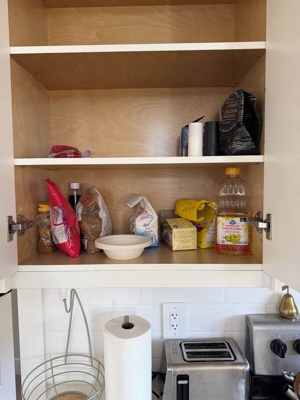 Una despensa de cocina con estantes llenos de diversos alimentos, incluyendo sacos de arroz, una botella de aceite y un cartón de leche.