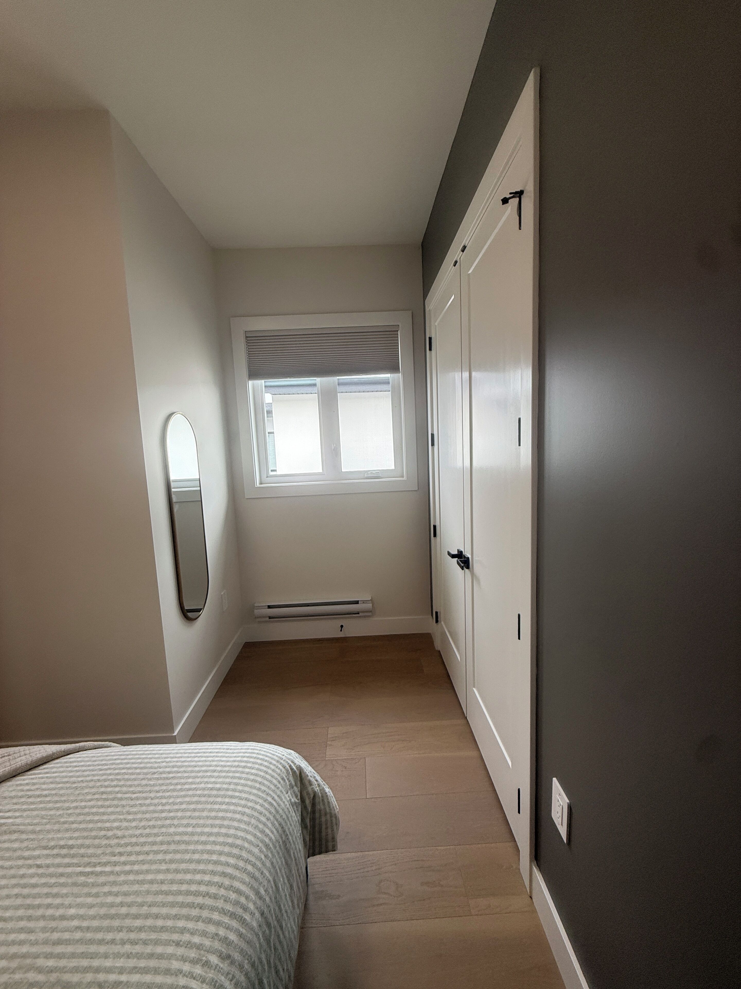 A bedroom with a bed, a window, a radiator, and a wardrobe.