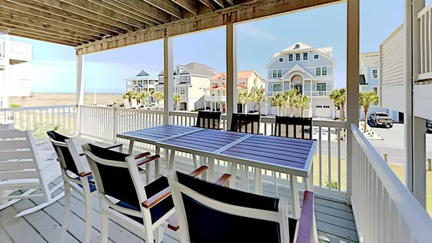 Un espace extérieur abrité, doté d’une table et de chaises, qui offre une vue sur la plage et les maisons qui s’y trouvent.