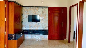 Una stanza con pavimento in marmo, un armadio in legno, una TV fissata al muro e una porta rossa.