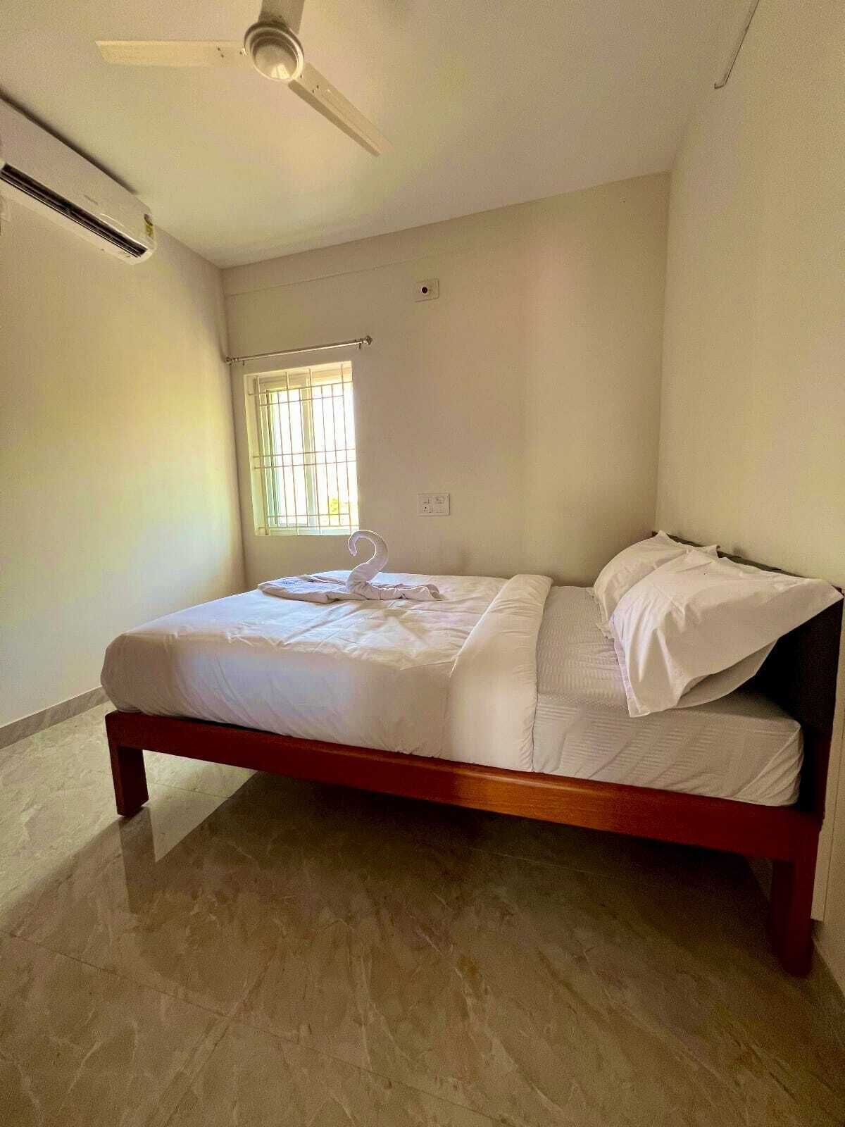 A single bed in a room with a ceiling fan, a window with bars, and a light switch on the wall.