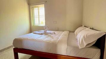 A single bed in a room with a ceiling fan, a window with bars, and a light switch on the wall.