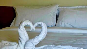 Ein Hotelzimmer mit einem ordentlich bezogenen Bett, weißen Leinentüchern und einer herzförmigen Handtuchdeko auf dem Bett.