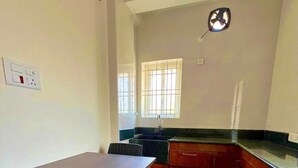 Una piccola cucina con un tavolo e sedie, una finestra con sbarre e una sveglia appesa al muro.