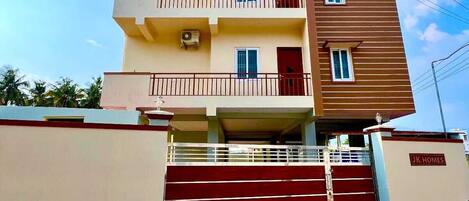 Un edificio residencial de varios pisos con balcones, una entrada con reja y un cartel que indica que es propiedad de J.K. Homes.