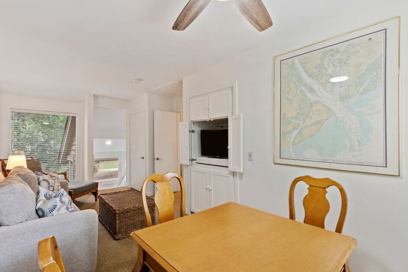 A living room with a wooden table, chairs, a TV, and a map on the wall.