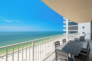 A balcony with a view of the ocean, a table, chairs, and a white railing. - New Luxury Gulf Front Phoenix Gulf Shores II 1501 (Gulf Shores)
