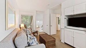 Een moderne woonkamer met een bank, een televisie en een rieten poef.