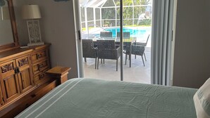 Un dormitorio con una cama grande, cómoda de madera y vistas a una zona de piscina exterior a través de una puerta corrediza de vidrio.