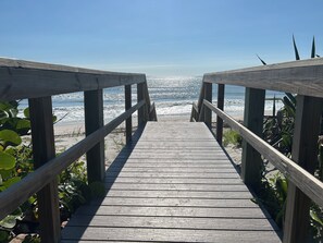 En træpromenade der fører hen til en strand med udsigt over havet.