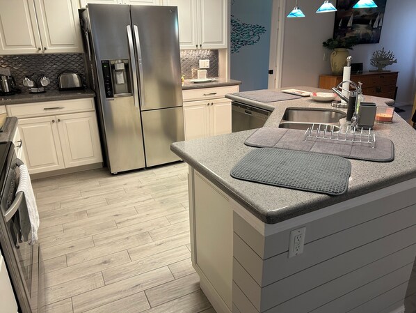 A modern kitchen with a stainless steel refrigerator, a built-in dishwasher, and a granite countertop.
