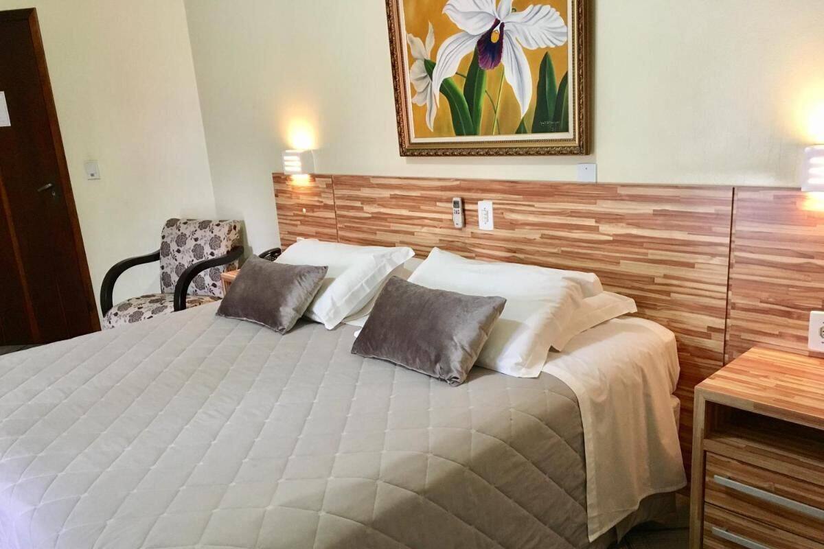 Una cama bien hecha con cubrecama acolchado, dos mesitas de noche con lámparas, y una obra de arte floral enmarcada sobre la cama.