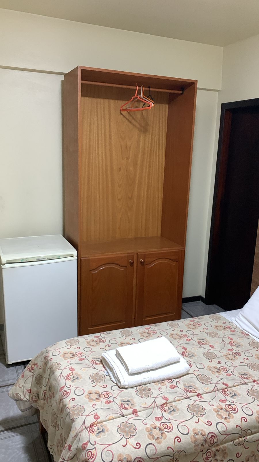 Un dormitorio con un armario de madera, una cama con colcha estampada y una mesita de noche blanca.