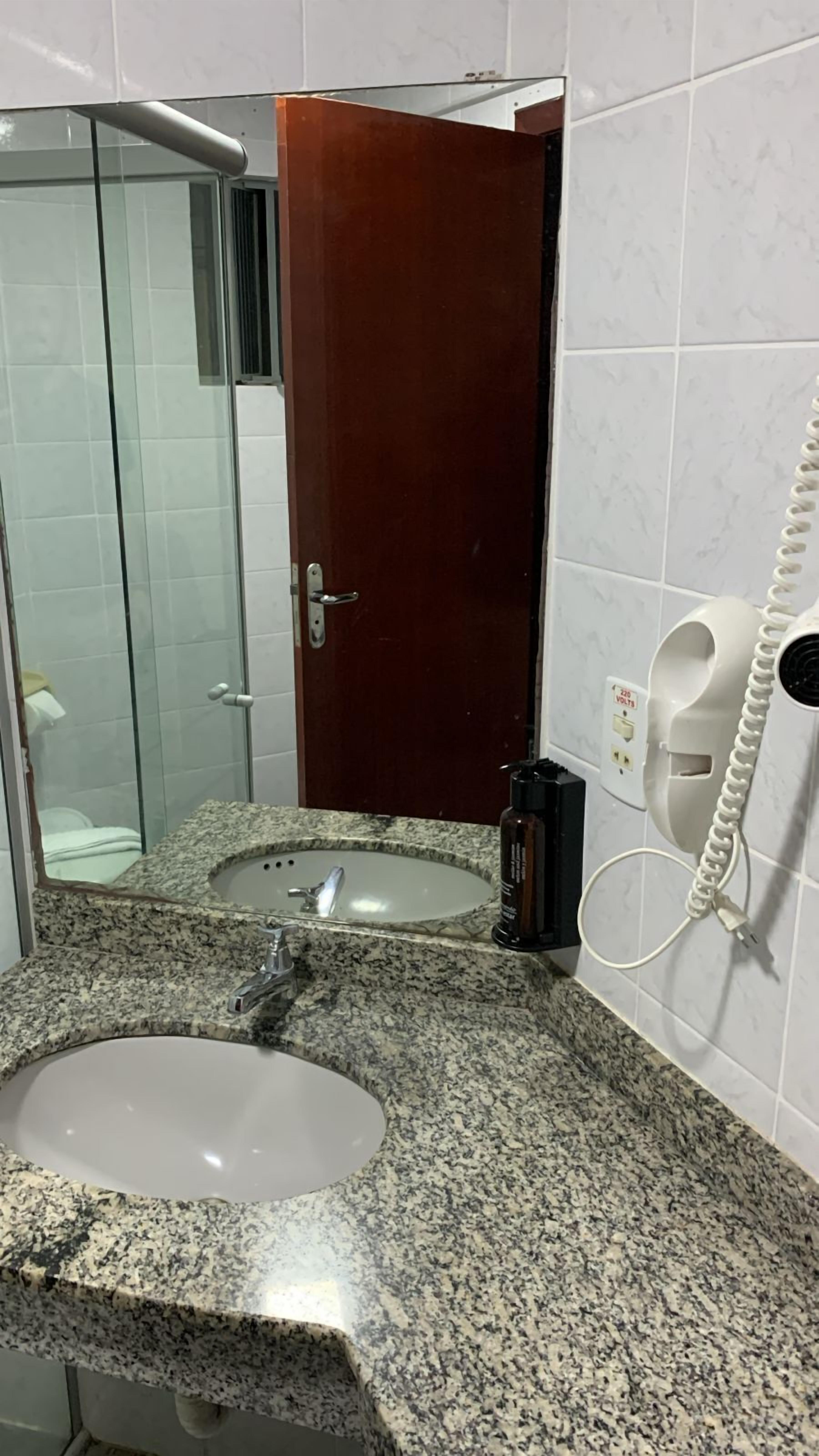 A bathroom with a granite countertop sink, a mirror, a wooden door, and a telephone.