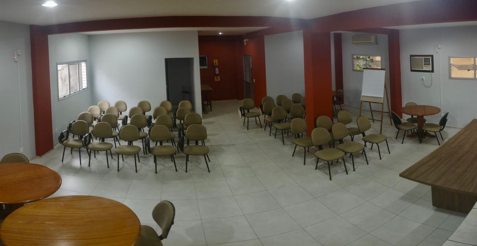Un salón de conferencias con varias filas de sillas y una mesa larga, paredes blancas y piso de baldosas.