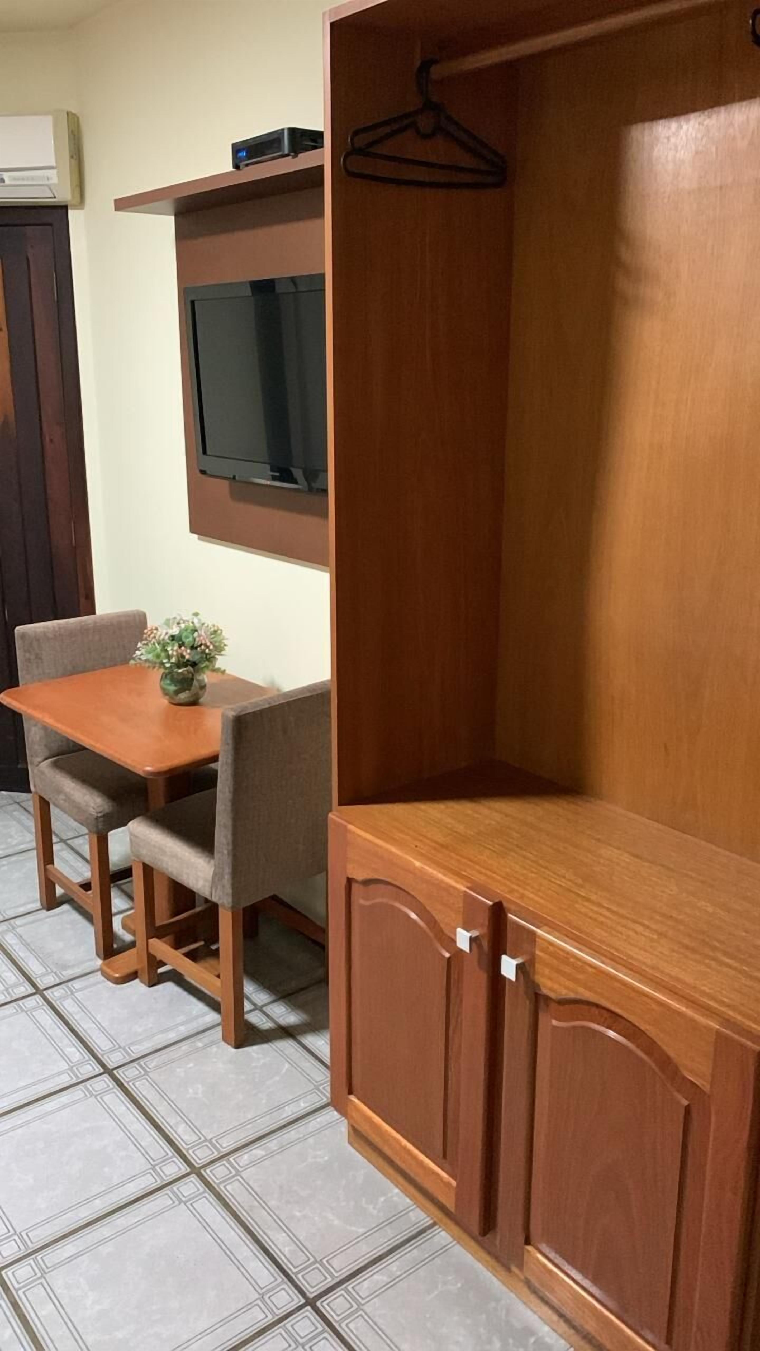 Un meuble en bois avec un téléviseur fixé au-dessus, une petite table avec des chaises et un porte-manteau suspendu.