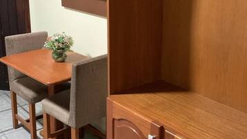 Un meuble en bois avec un téléviseur fixé au-dessus, une petite table avec des chaises et un porte-manteau suspendu.