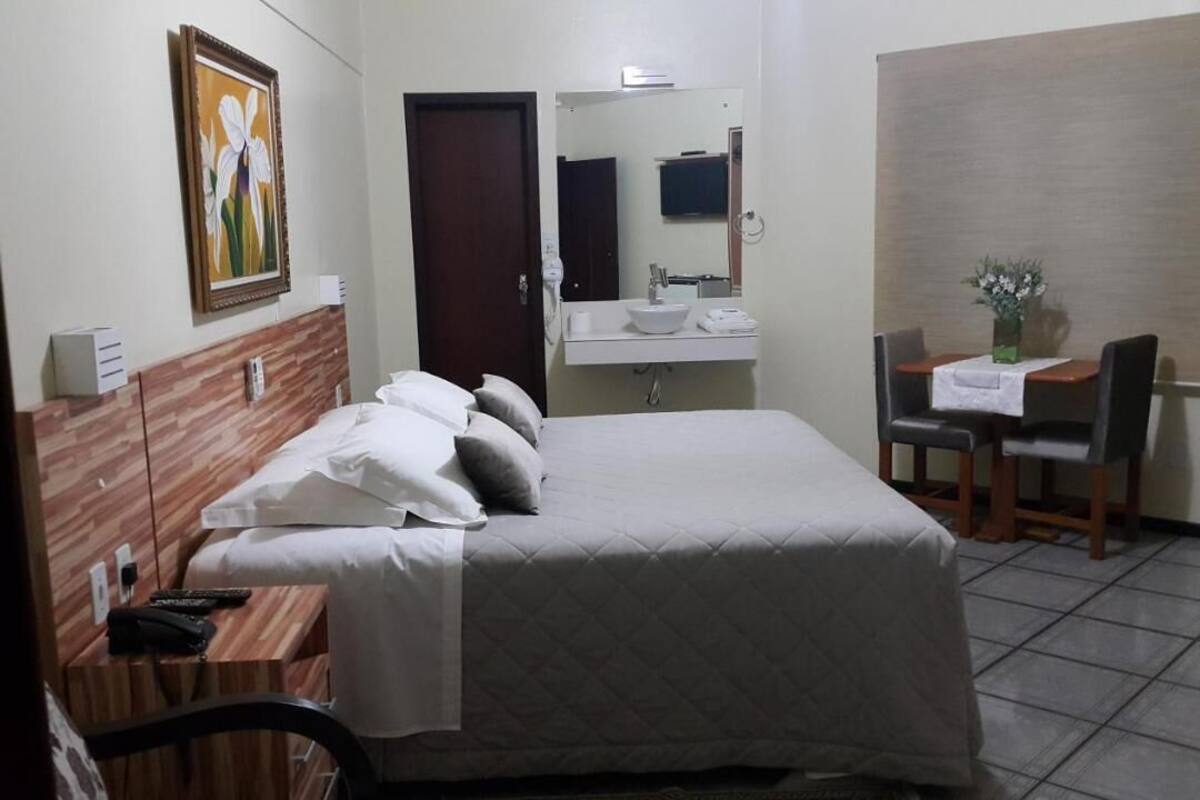 Una habitación de hotel con cama, mesita de noche, espejo, lavamanos y una pequeña mesa de comedor con sillas.