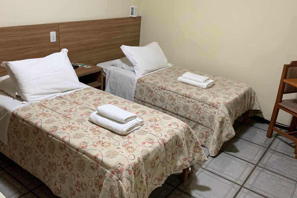 Dos camas individuales con colchas estampadas, almohadas blancas y toallas dobladas con cuidado.