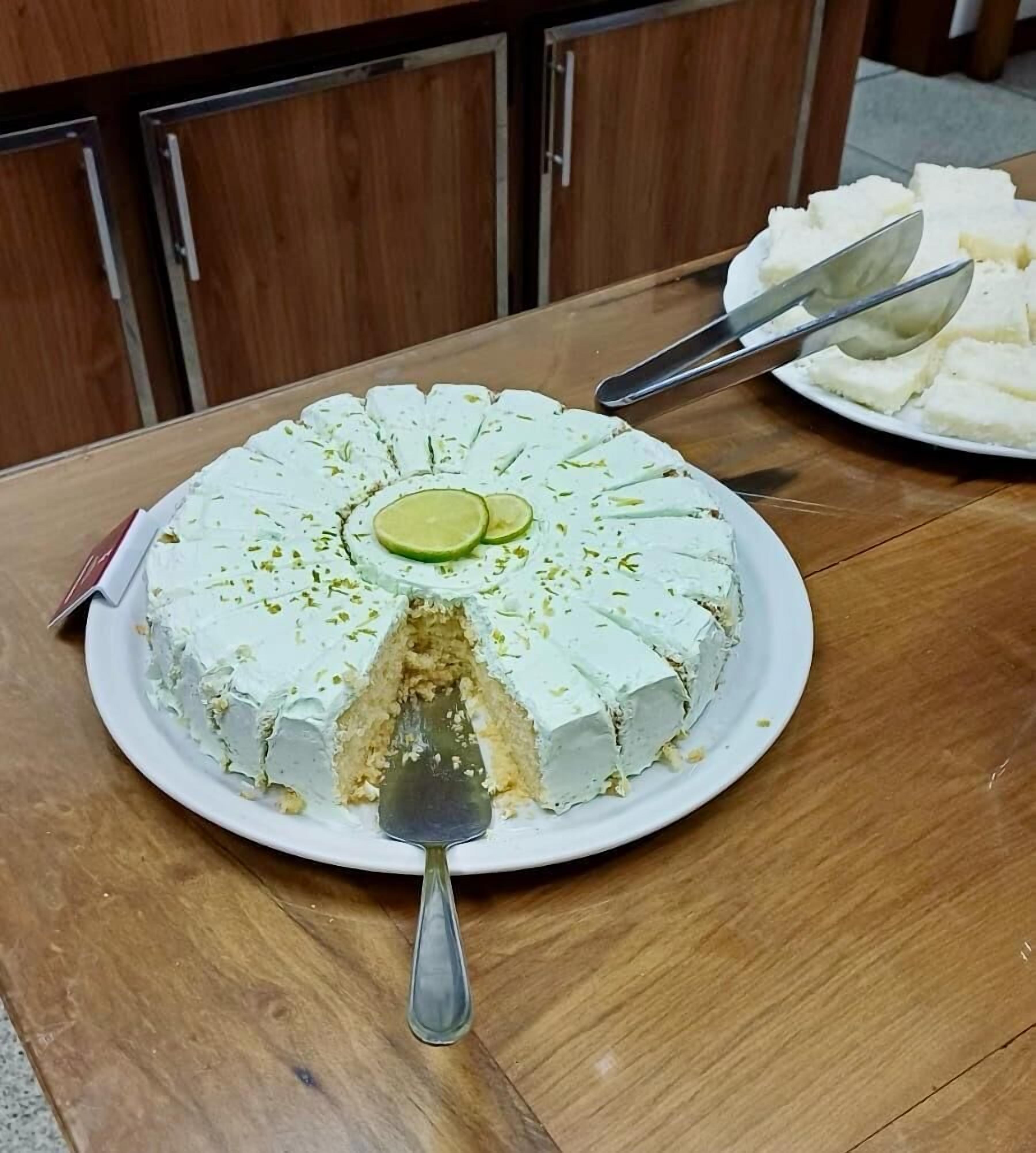 A round cake with lime slices on top, placed on a white plate with a serving spoon.