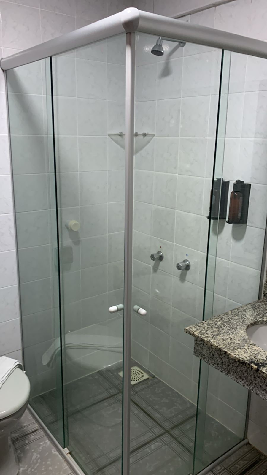 Cabina de ducha con paredes de azulejos blancos, encimera de granito y un inodoro a la izquierda.