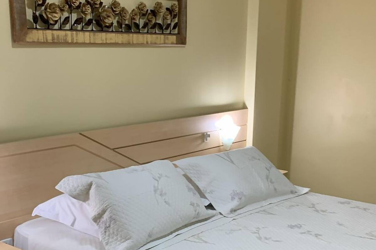 Un dormitorio con cama, mesita de noche, alfombra floral y un adorno en la pared.