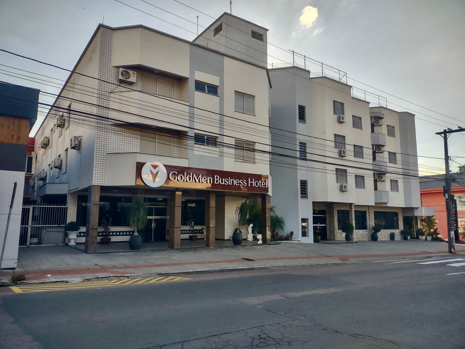 Un hotel llamado GoldMen Business Hotel con una fachada moderna, varios pisos y una entrada destacada con un letrero.