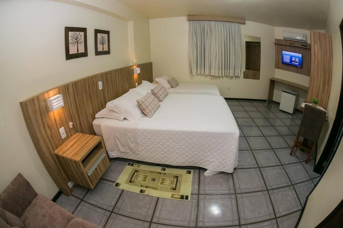 Habitación de hotel con una cama grande, un escritorio pequeño, un televisor y un ventanal con cortinas.