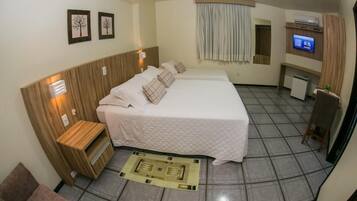 A hotel room with a large bed, a small desk, a TV, and a window with curtains.