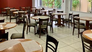 A restaurant with multiple round tables and chairs, wooden ceiling, and large windows with a view of greenery. - Goldmen Business Criciúma (Criciuma)