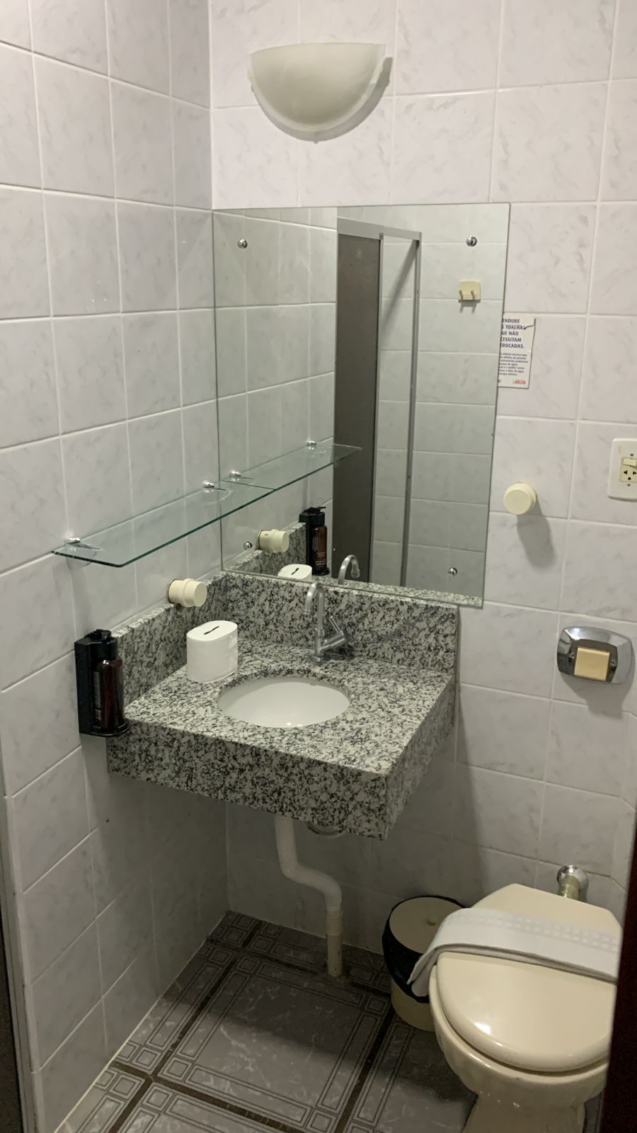 A compact bathroom with a granite sink, a glass shelf, a mirror, a toilet, and a shower area.