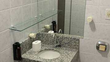 A compact bathroom with a granite sink, a glass shelf, a mirror, a toilet, and a shower area.