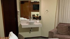 A hotel room with a bed, a sofa, a bathroom with a sink, and a television. - Goldmen Business Criciúma (Criciuma)