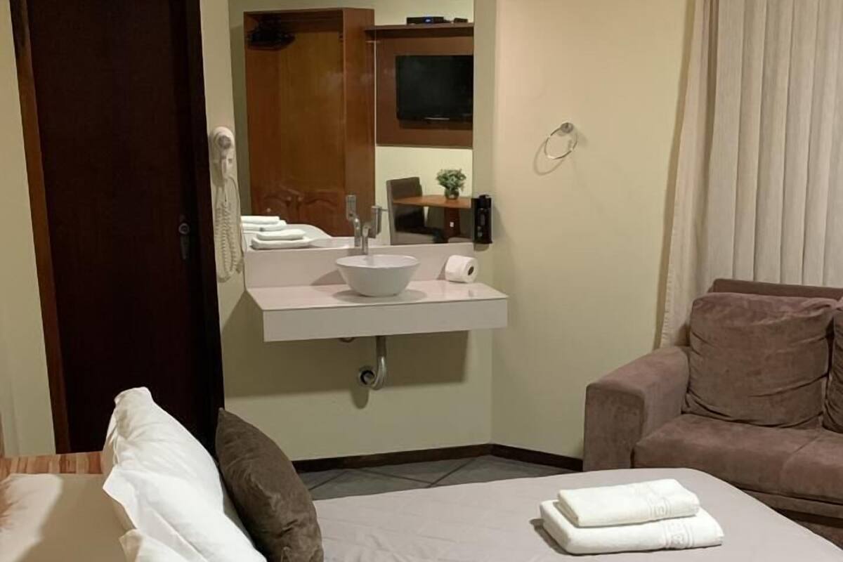 Habitación de hotel con cama, sofá, baño con lavamanos y televisión.