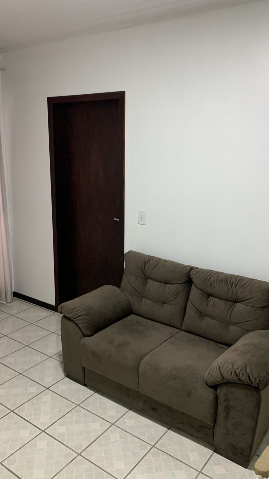 Ein Zimmer mit einer dunklen Holztür, einem braunen Sofa und einem Fliesenboden.