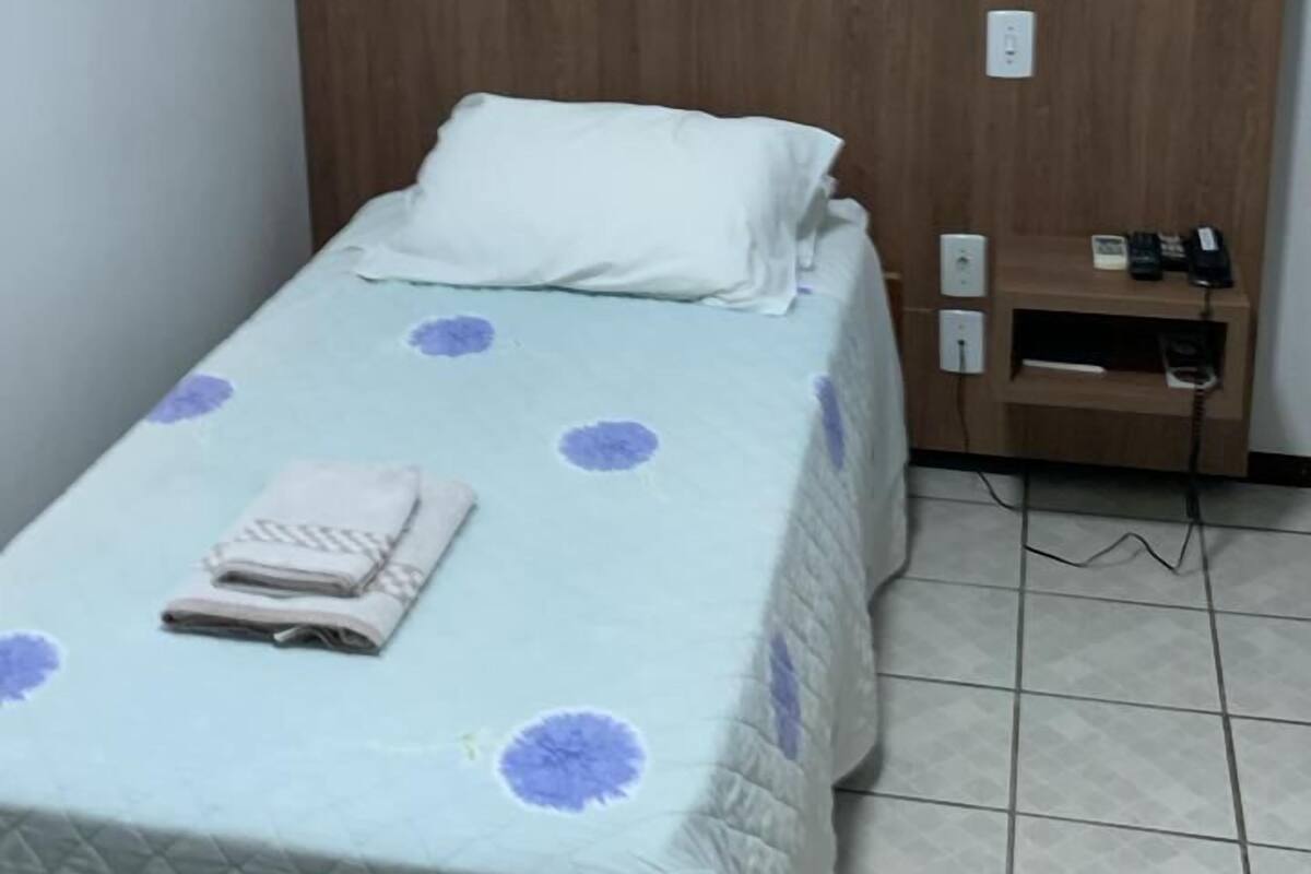 Una habitación pequeña con cama individual, cabecera de madera, mesita de noche con teléfono y toma de corriente.