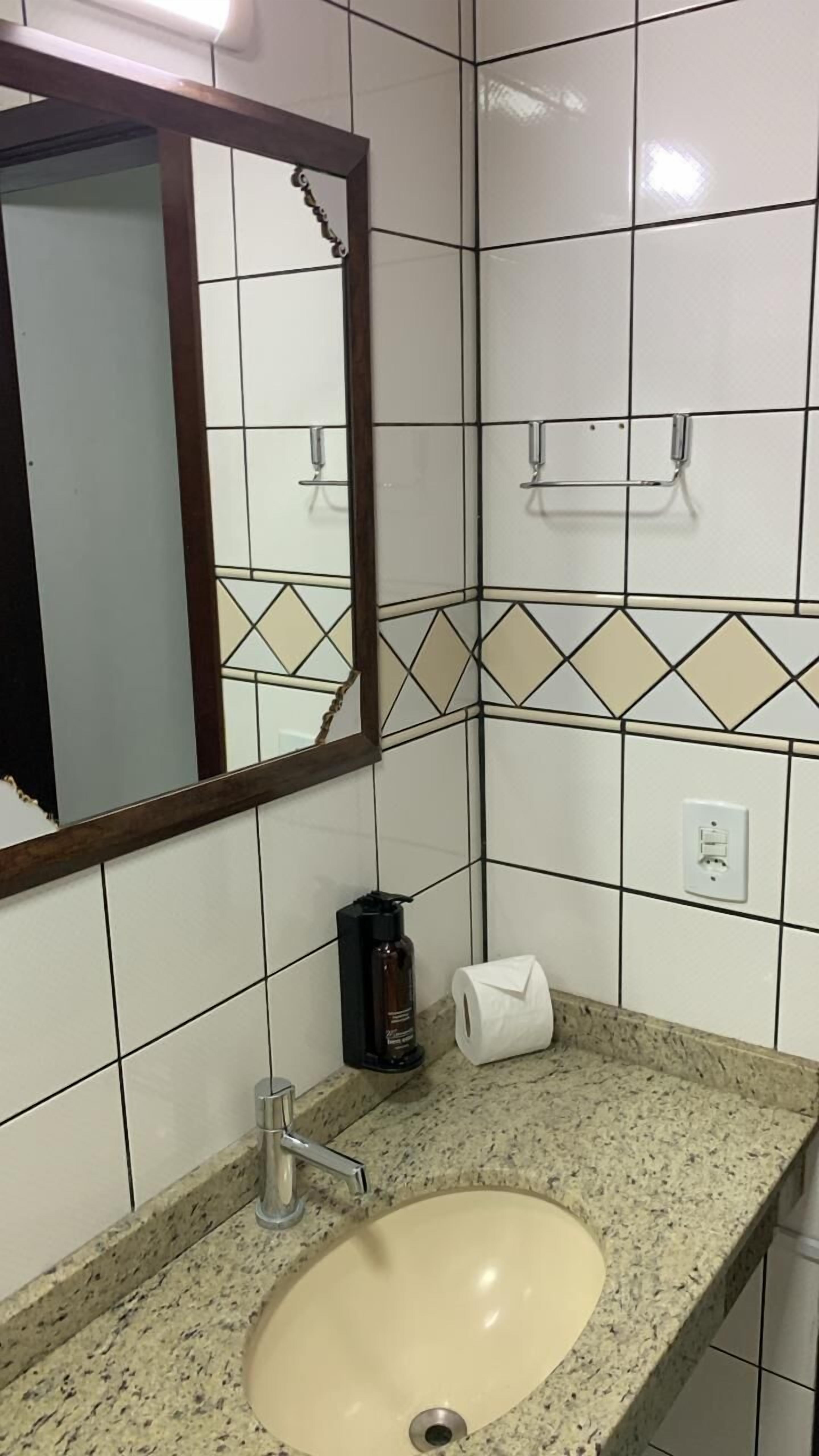 Un baño con lavamanos, espejo y paredes de azulejos.